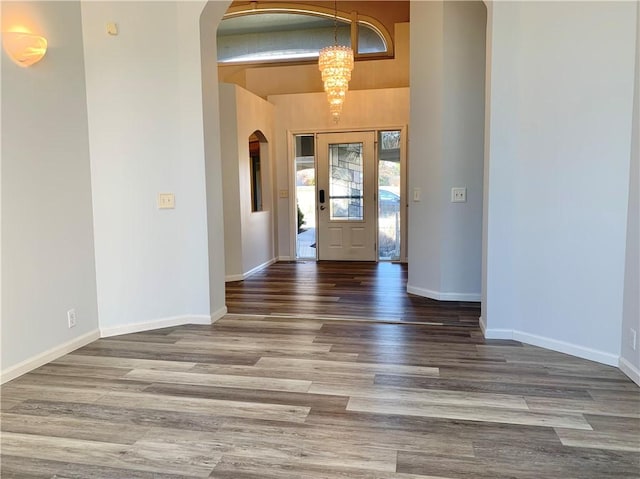 foyer featuring arched walkways, an inviting chandelier, baseboards, and wood finished floors