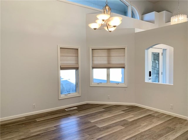 spare room featuring a chandelier, visible vents, a towering ceiling, and wood finished floors