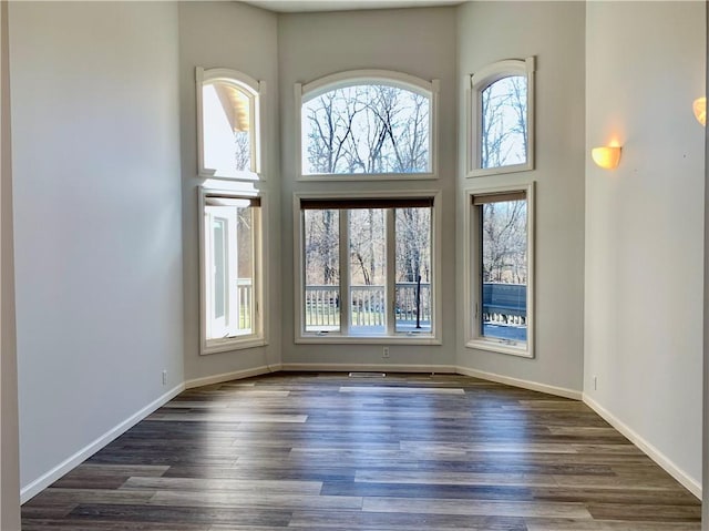 unfurnished room with a high ceiling, dark wood-style flooring, and baseboards