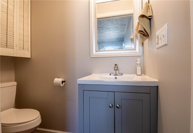 half bathroom with vanity, toilet, and baseboards