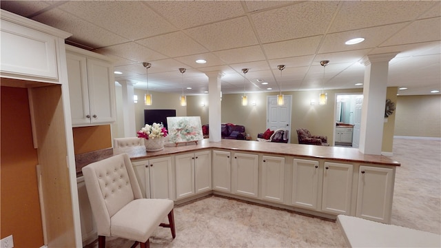 kitchen featuring pendant lighting, decorative columns, white cabinets, kitchen peninsula, and a drop ceiling