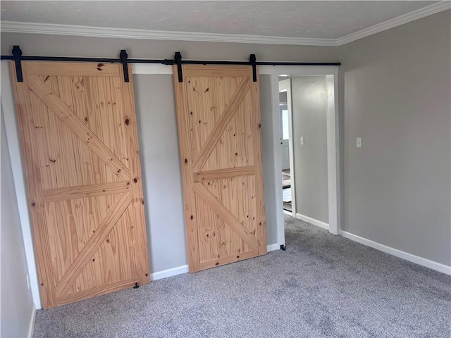 carpeted spare room with crown molding, baseboards, and a barn door