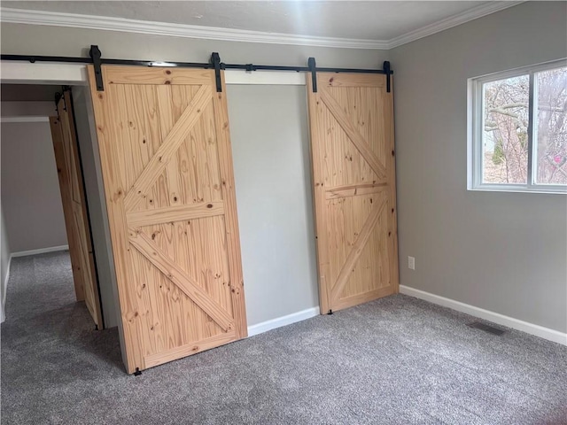 unfurnished bedroom featuring baseboards, a barn door, carpet, and crown molding