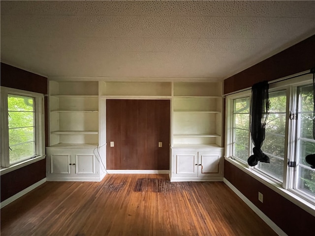 spare room featuring built in shelves, dark hardwood / wood-style flooring, and a textured ceiling