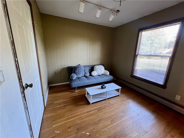 living area featuring wood-type flooring, baseboard heating, wooden walls, and track lighting