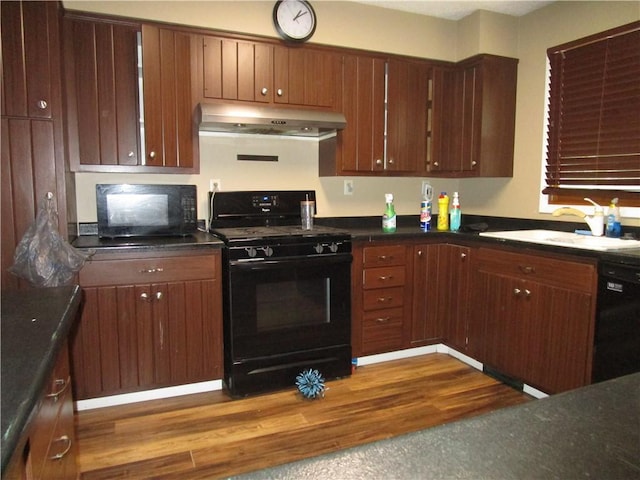 205 Franklin St, Pana, IL 62557 - kitchen featuring black appliances, under cabinet range hood, a sink, dark countertops, and dark wood finished floors