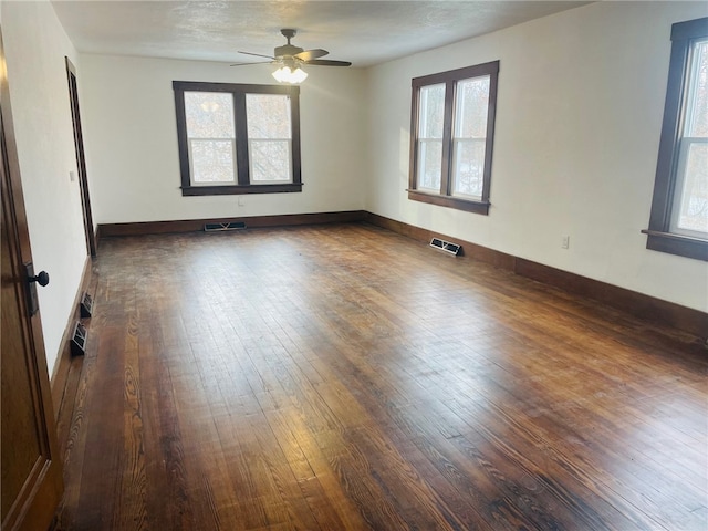 empty room with ceiling fan, plenty of natural light, and dark hardwood / wood-style floors