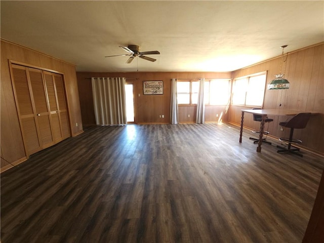 unfurnished living room with dark wood-type flooring, wood walls, and a ceiling fan