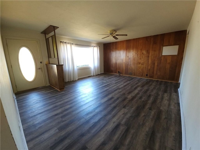 unfurnished living room with dark wood-style flooring, ceiling fan, wooden walls, and baseboards