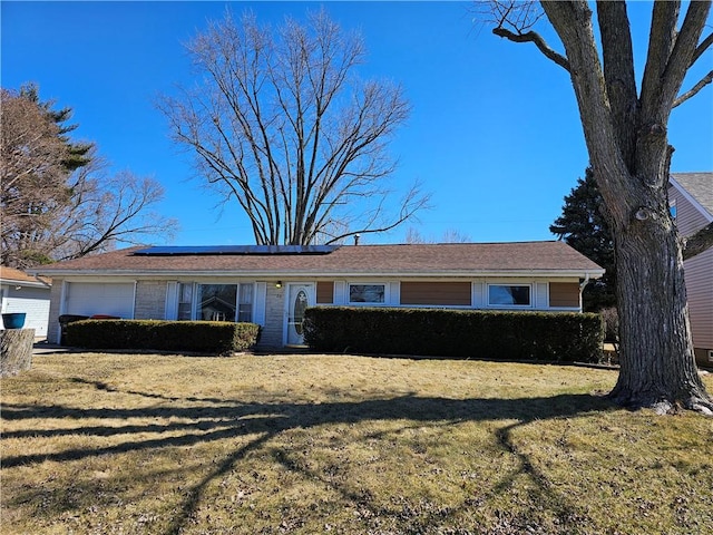 ranch-style home with a front yard, brick siding, an attached garage, and solar panels