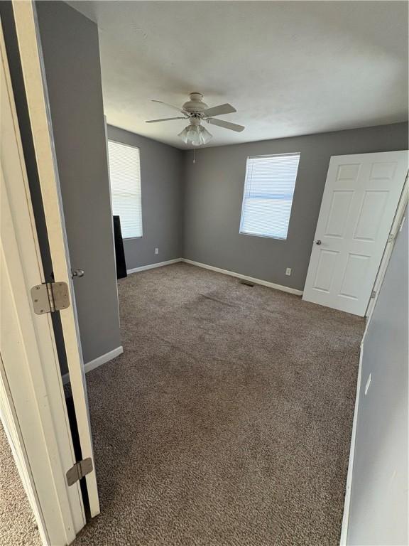 unfurnished bedroom with multiple windows, dark carpet, visible vents, and baseboards