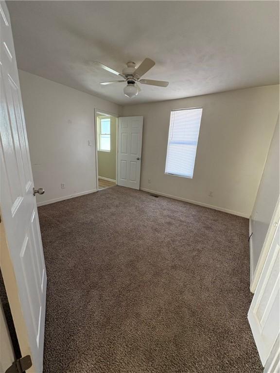 empty room featuring baseboards, dark carpet, and a ceiling fan