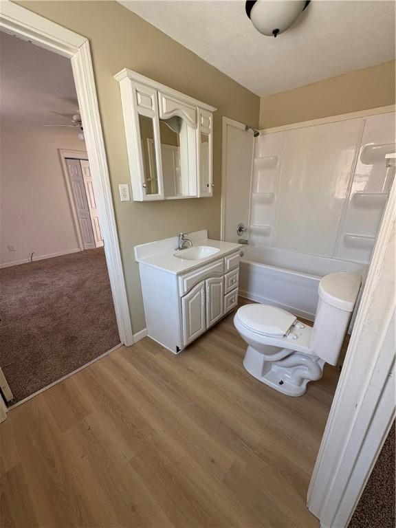 full bath with bathtub / shower combination, toilet, vanity, wood finished floors, and baseboards