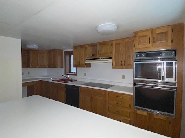 kitchen with under cabinet range hood, brown cabinetry, a sink, black appliances, and light countertops
