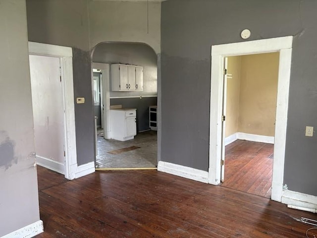 spare room featuring arched walkways, wood-type flooring, baseboards, and a smoke detector
