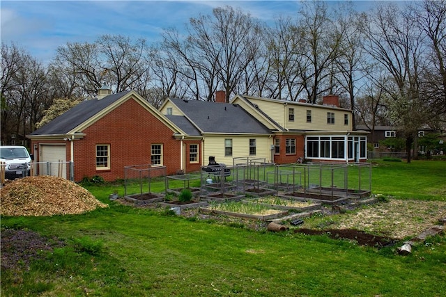 rear view of house featuring an attached garage, brick siding, a sunroom, a chimney, and a garden