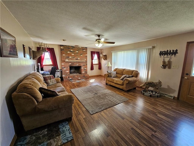 living room featuring a ceiling fan, a brick fireplace, wood finished floors, and a textured ceiling