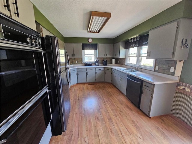 kitchen with a sink, light wood-style floors, black appliances, and light countertops