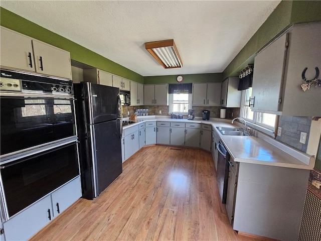 kitchen with light wood-style floors, backsplash, black appliances, and light countertops