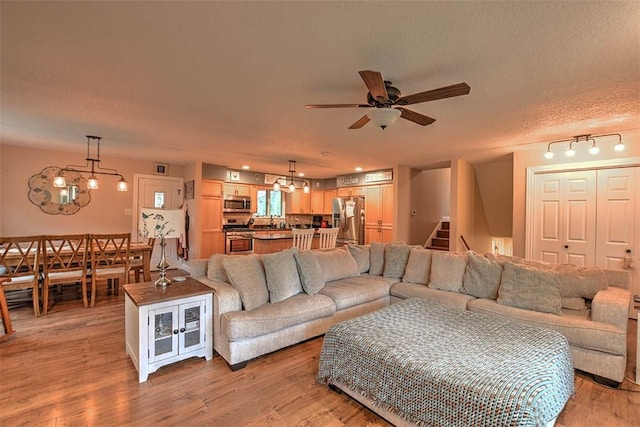 living room with ceiling fan with notable chandelier, a textured ceiling, and light wood-type flooring