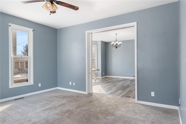 carpeted empty room featuring ceiling fan with notable chandelier