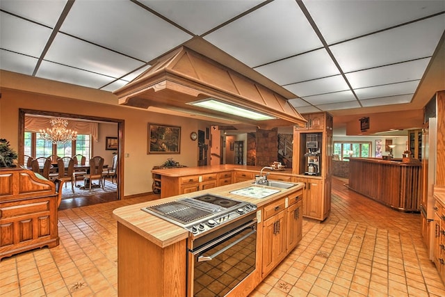 kitchen featuring sink, a notable chandelier, stainless steel stove, butcher block counters, and an island with sink