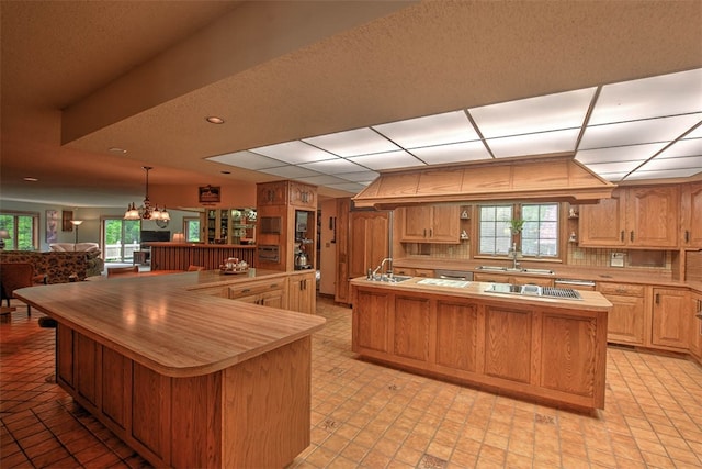 kitchen with tasteful backsplash, a notable chandelier, pendant lighting, stainless steel gas stovetop, and a kitchen island with sink