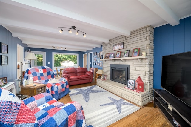 living room with beamed ceiling, wood-type flooring, and a stone fireplace