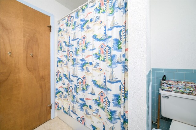 bathroom with a shower with curtain, toilet, tile walls, and tile patterned floors