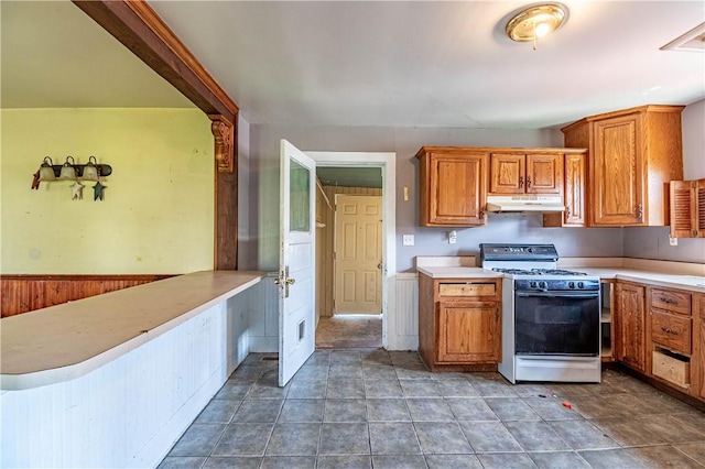 kitchen with brown cabinets, wooden walls, light countertops, white gas stove, and under cabinet range hood