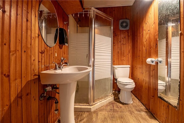 bathroom with wood walls, a shower stall, toilet, and wood finished floors