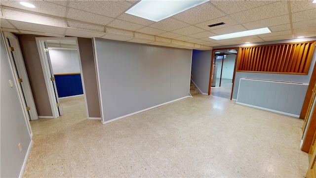 finished below grade area with a paneled ceiling, baseboards, stairway, and tile patterned floors