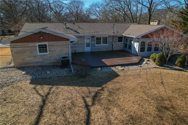 back of house with a lawn, stone siding, roof with shingles, a deck, and cooling unit