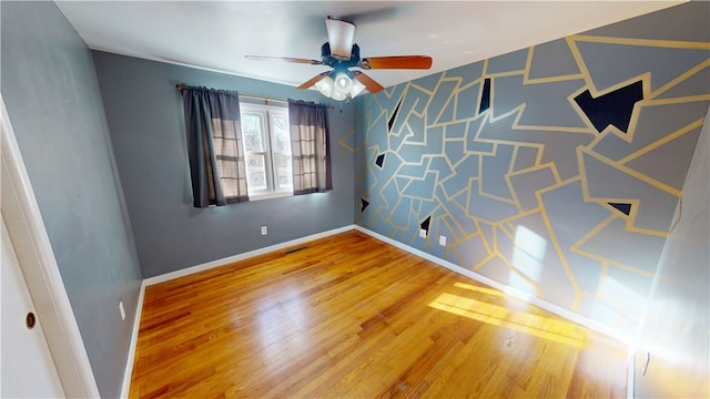 spare room featuring visible vents, an accent wall, a ceiling fan, wood finished floors, and baseboards