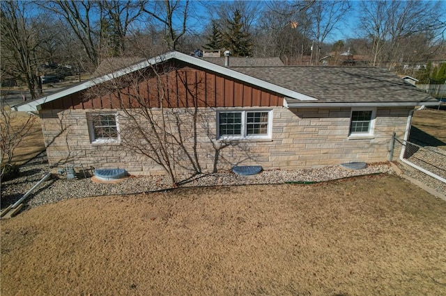 view of property exterior with a shingled roof, a lawn, board and batten siding, fence, and stone siding