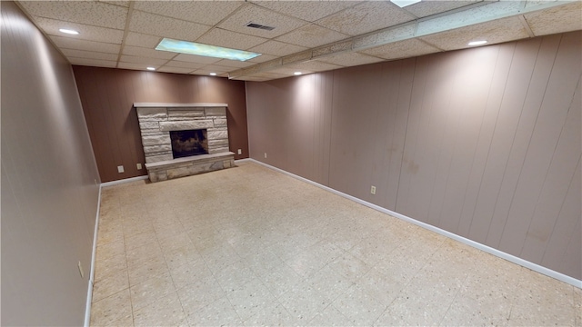 unfurnished living room with a paneled ceiling, baseboards, a stone fireplace, and tile patterned floors