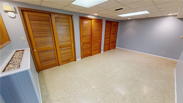 unfurnished bedroom featuring visible vents, a drop ceiling, two closets, and tile patterned floors