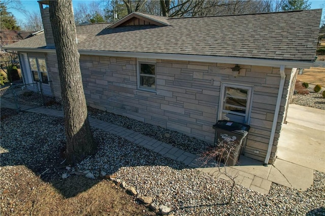 view of home's exterior with stone siding, a shingled roof, and a chimney