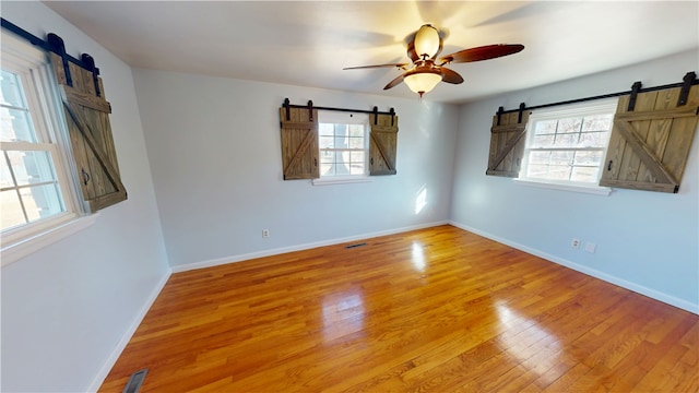 unfurnished room featuring a healthy amount of sunlight, a barn door, and wood finished floors