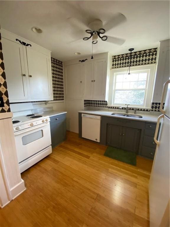 kitchen with white appliances, white cabinets, sink, hanging light fixtures, and light hardwood / wood-style flooring