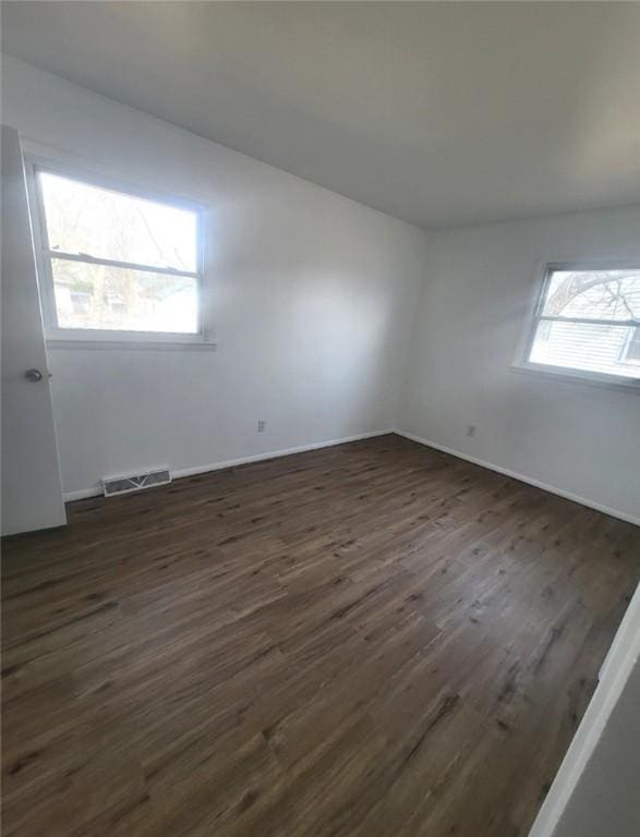 spare room with dark wood-style floors, visible vents, and a healthy amount of sunlight