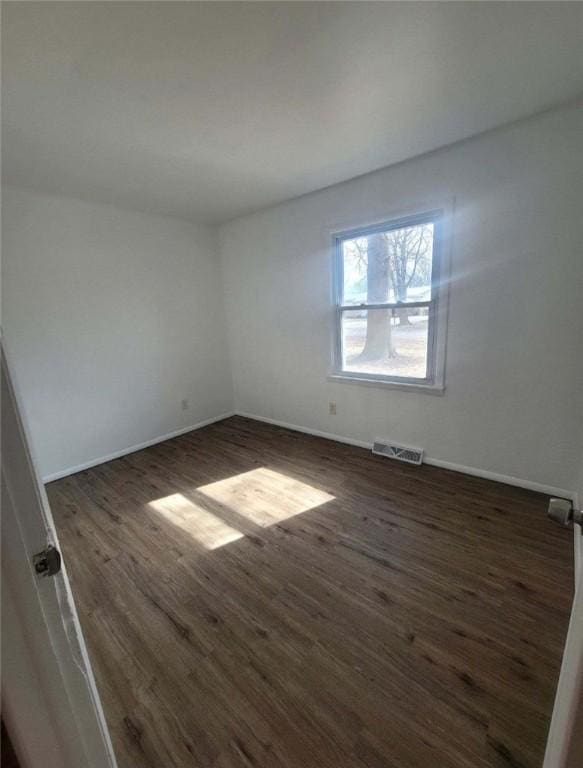 spare room with wood finished floors, visible vents, and baseboards