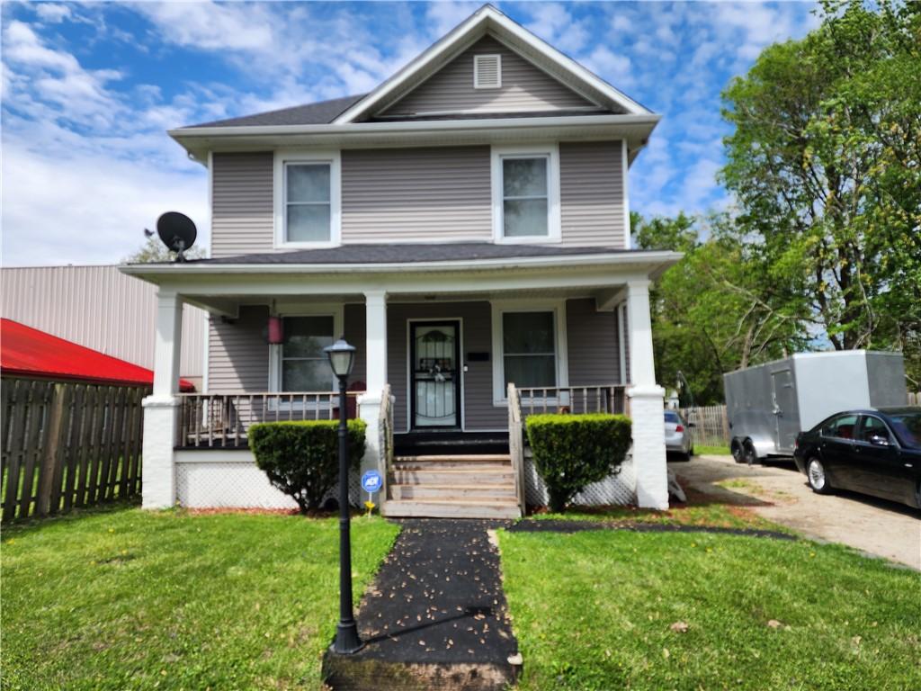 american foursquare style home featuring a front lawn, fence, and covered porch
