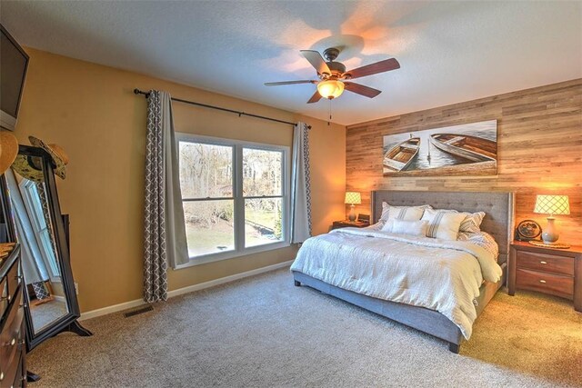 bedroom with carpet, a textured ceiling, ceiling fan, and wood walls