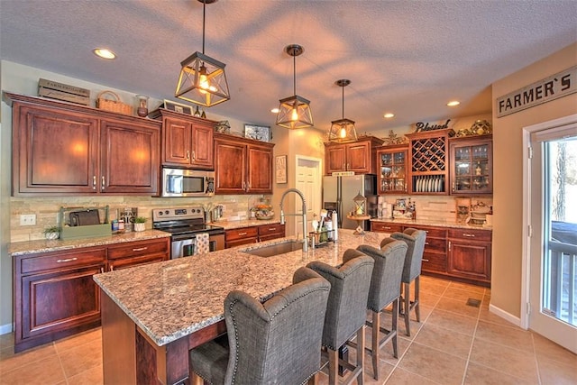 kitchen with pendant lighting, a breakfast bar area, a kitchen island with sink, light tile patterned floors, and stainless steel appliances