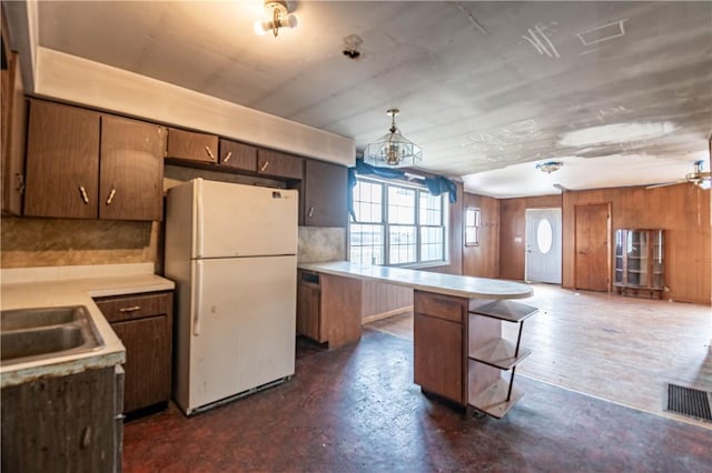 kitchen with white fridge, a kitchen bar, sink, wood walls, and hanging light fixtures