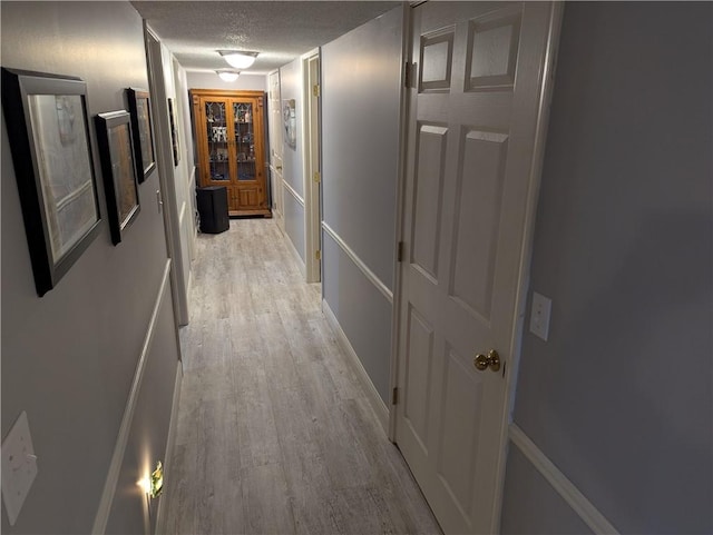 corridor with light wood finished floors and a textured ceiling