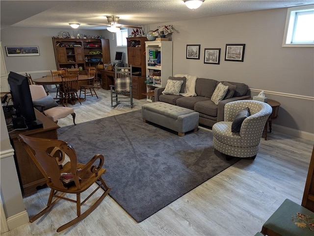 living room featuring baseboards, a textured ceiling, a ceiling fan, and wood finished floors