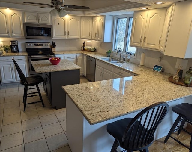 kitchen with a peninsula, a sink, stainless steel appliances, white cabinetry, and a kitchen breakfast bar