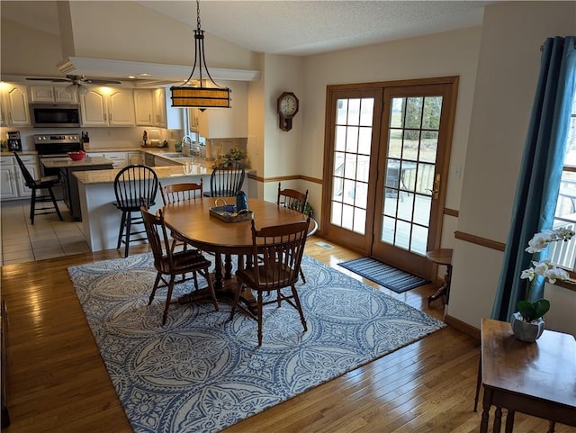 dining space with a textured ceiling, baseboards, light wood-style floors, and vaulted ceiling